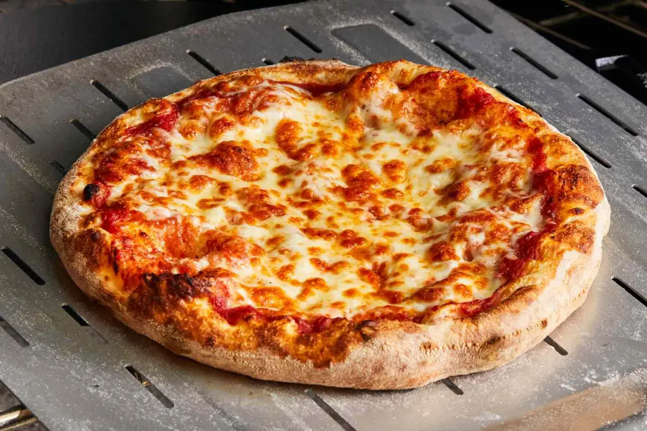 Gorąca pizza z ciągnącym się serem na łopacie. Idealny ser na pizze, który apetycznie się rozpływa.