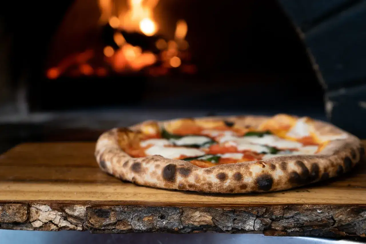 Pyszna pizza margherita na drewnianej desce, w tle żar z pieca. Idealna do pieca z termoobiegiem.