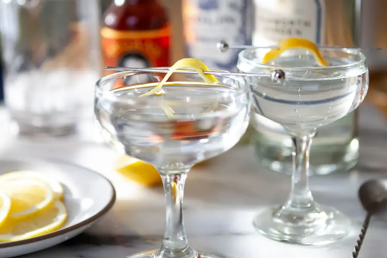 Dwa eleganckie kieliszki z drinkami, idealne na wieczór. Martini wstrząśnięte nie mieszane, ozdobione skórką cytrynową.