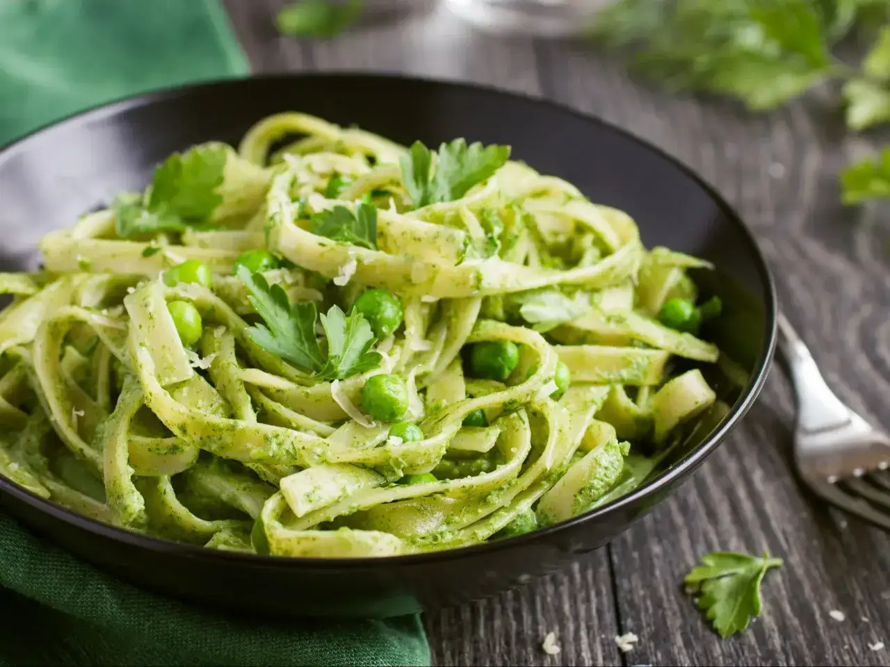 Pyszny makaron z pesto ze słoika, z groszkiem i natką pietruszki, podany w czarnej misce na drewnianym blacie.