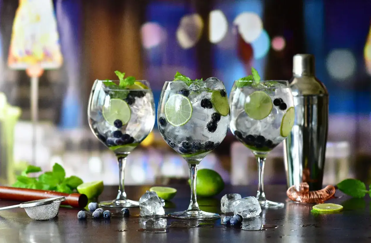 Trzy orzeźwiające gin z colą, udekorowane jagodami, limonką i miętą, gotowe do degustacji.