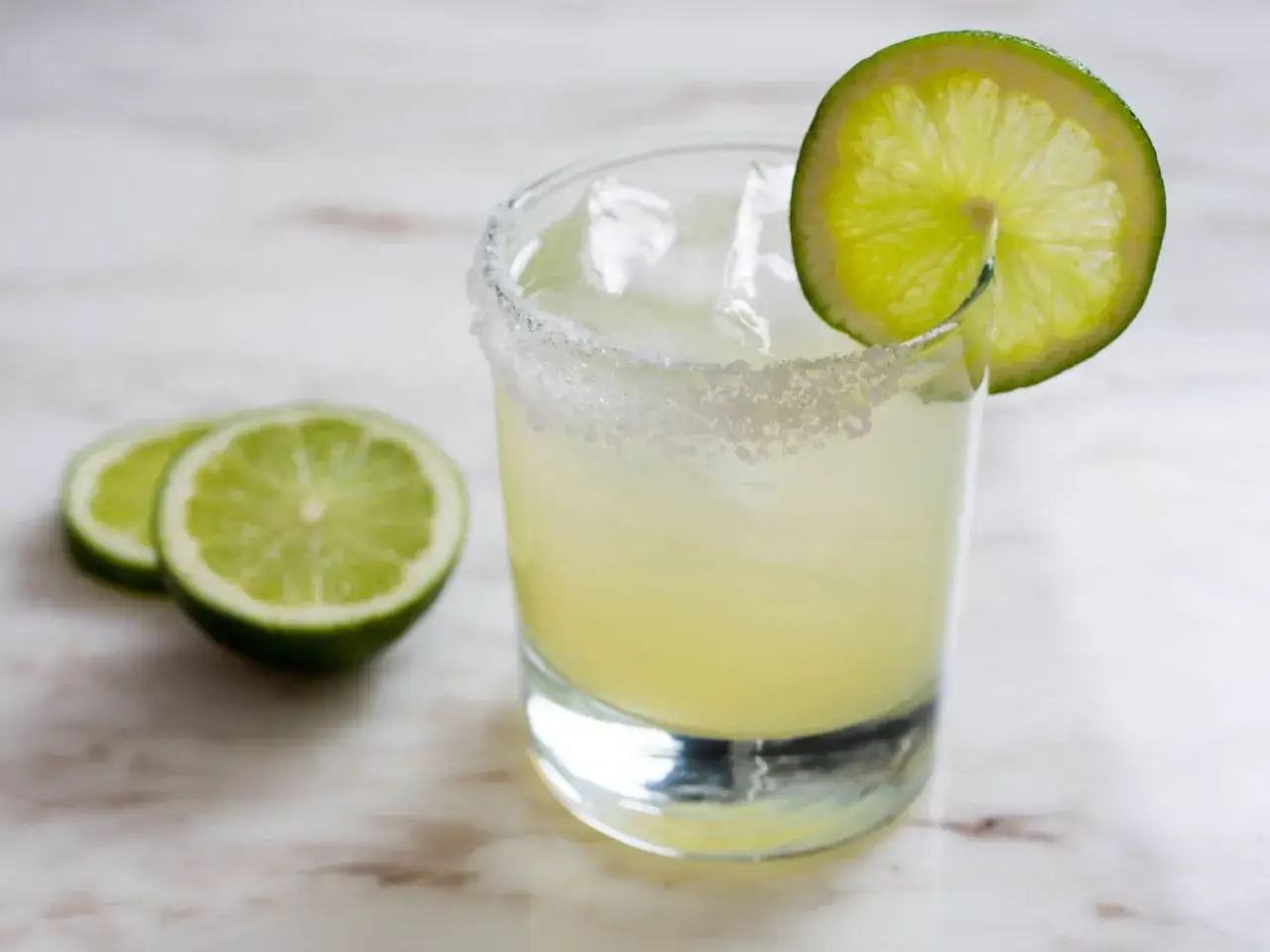 Orzeźwiająca margarita drink z lodem, solnym rantem i plasterkiem limonki. Obok leżą dwa plastry limonki.