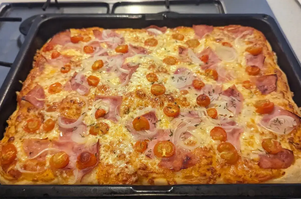Pyszna pizza z szynką, pomidorkami koktajlowymi i cebulą, prosto z pieca.