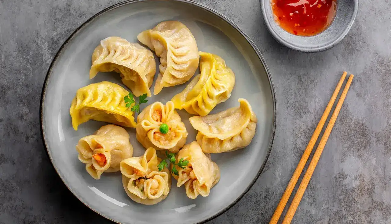 Talerz pełen pierożków dim sum, z czym podawać je? Obok miseczka z ostrym sosem i pałeczki.