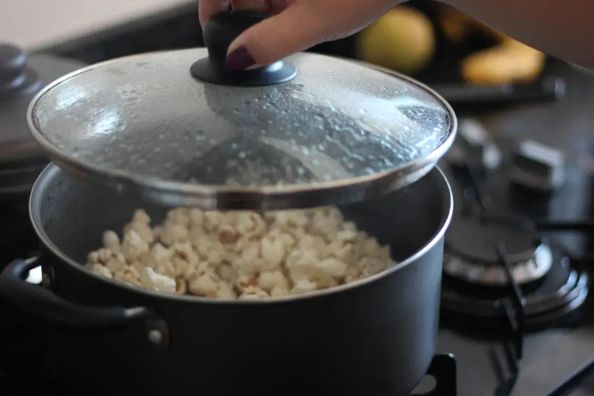 Ręka podnosi pokrywkę garnka, odsłaniając pyszny, świeżo zrobiony popcorn. Idealny sposób, jak zrobić popcorn na wieczór filmowy!
