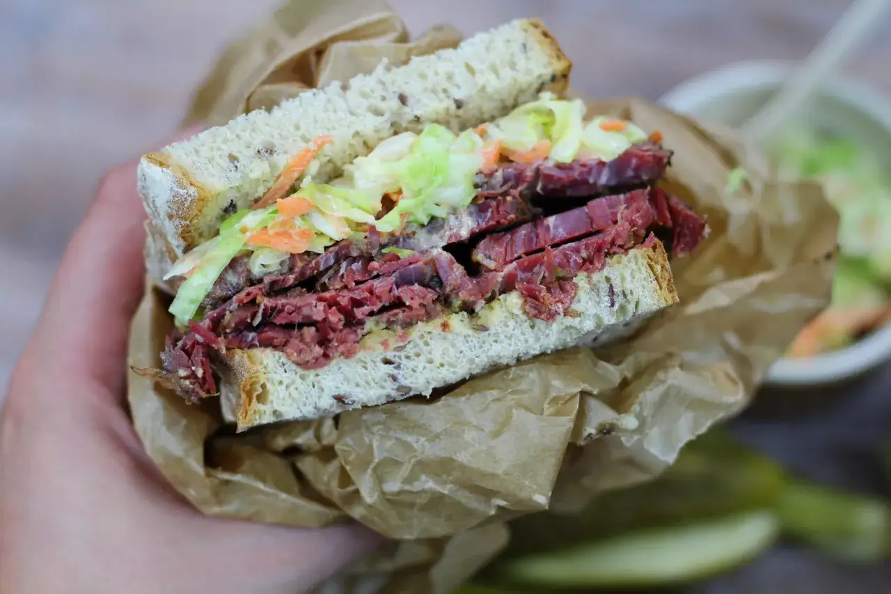 Pyszna kanapka z pastrami, z grubymi plastrami mięsa, chrupiącą surówką i musztardą, zawinięta w papier.