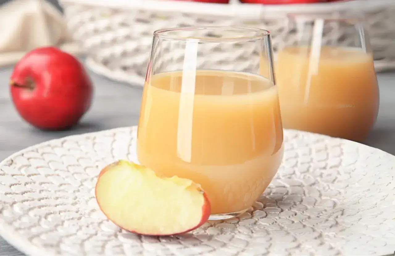 Orzeźwiający drink z sokiem jabłkowym, podany z kawałkiem jabłka na ozdobnym talerzyku.