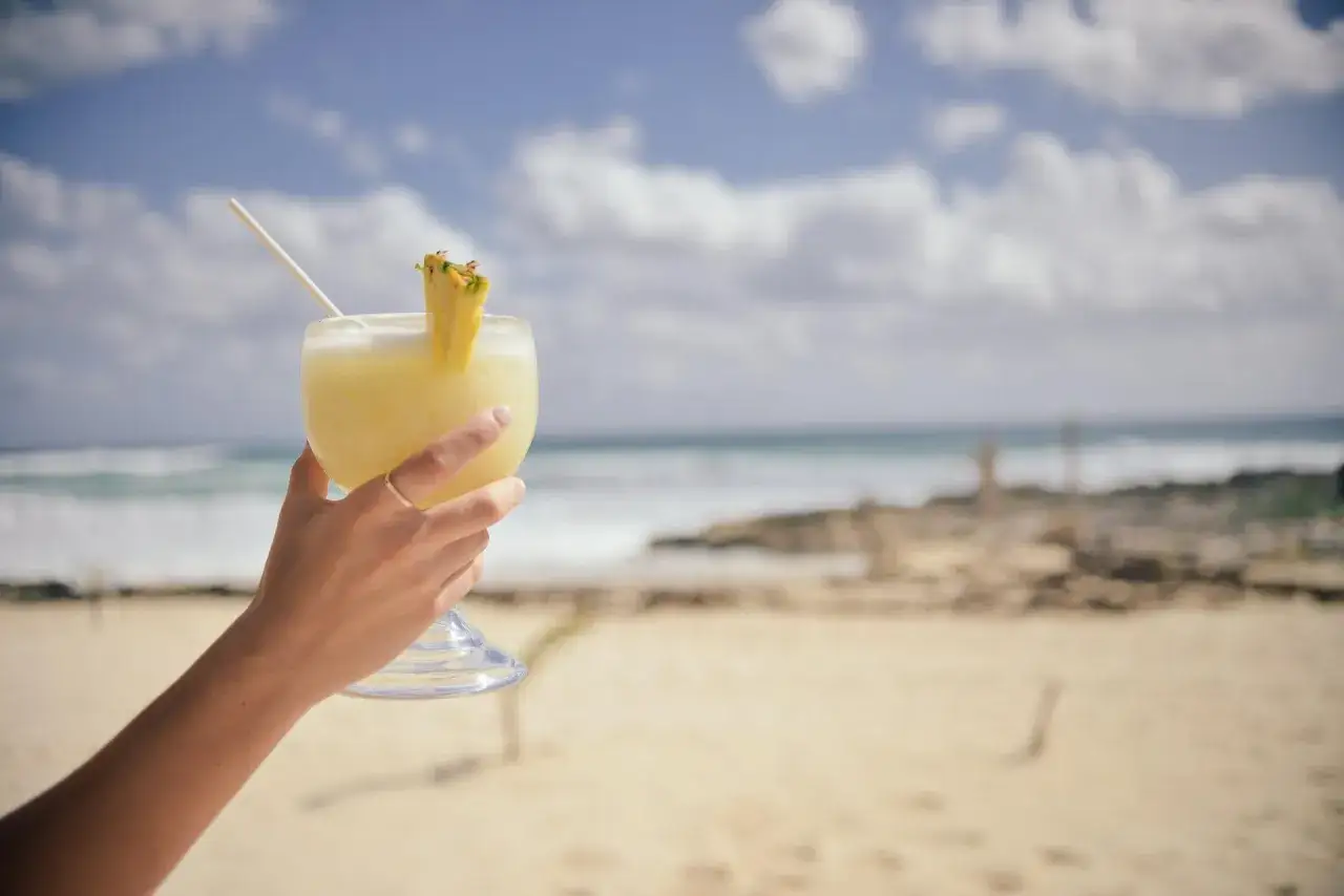 Ręka trzymająca orzeźwiający drink z ananasem na tle plaży i oceanu. Idealny na wakacje.