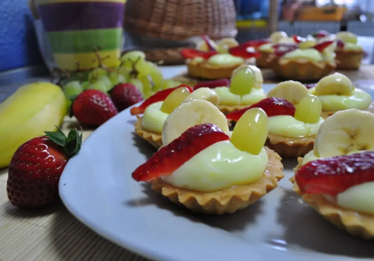 Pyszne babeczki z budyniem, udekorowane truskawkami, bananami i winogronami, wyglądają apetycznie.