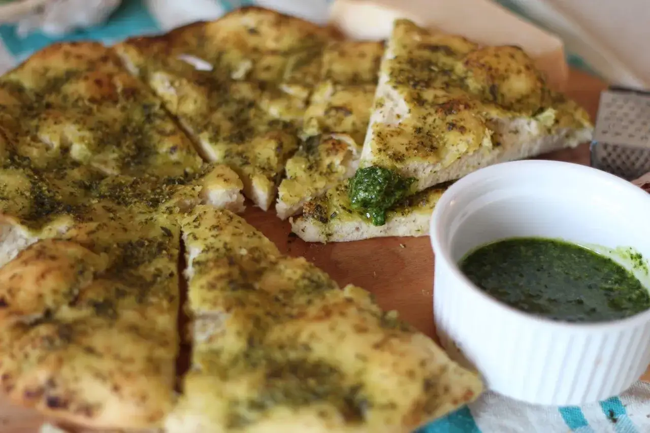 Pyszna focaccia z ziołami, pokrojona w trójkąty, gotowa do zanurzenia w aromatycznym dipie. Idealna przekąska.