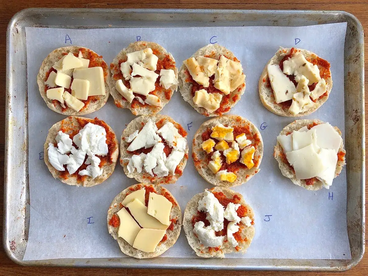 Mini pizze z różnymi rodzajami sera na spodzie z bułki. Każda porcja ma swój ser na pizze, od mozzarelli po żółty ser.