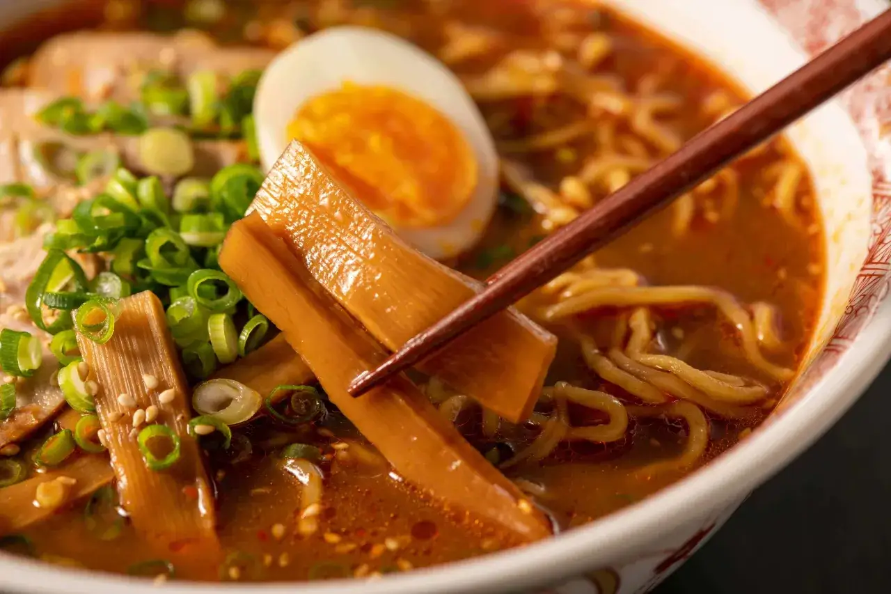 Chopsticks podnoszą pędy bambusa z miski ramenu, pełnej makaronu, jajka i zielonej cebulki. To idealne dodatki do ramenu.