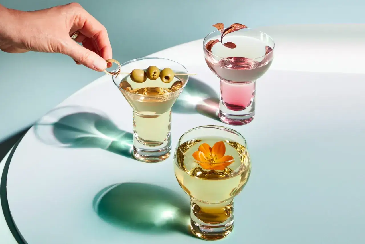 Eleganckie domowe drinki z wódką: martini z oliwkami, różowy koktajl i złoty z kwiatem.