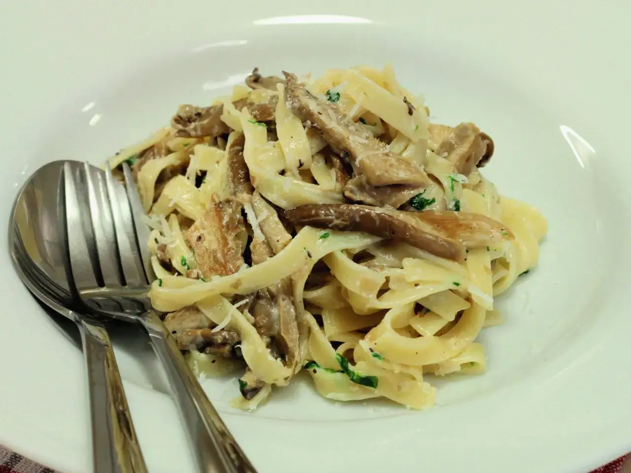 Pyszne fettuccine z boczniakami, posypane parmezanem i natką pietruszki, gotowe do podania z widelcem i łyżką.
