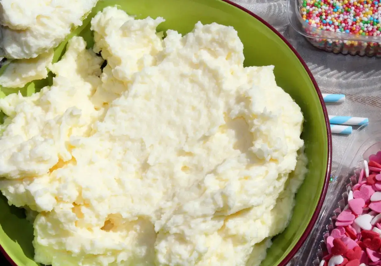 Puszysty krem budyniowy z mascarpone w zielonej misce, obok kolorowa posypka i serduszka. Idealny do deserów.