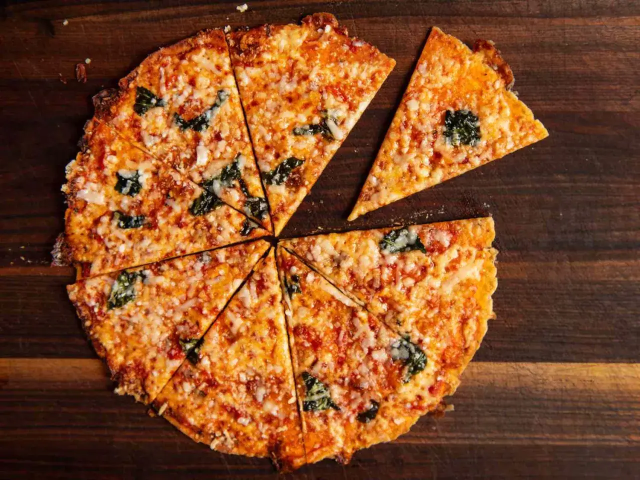 Chrupiąca pizza z tortilli, pokrojona w trójkąty, z roztopionym serem i zielonymi listkami, wygląda apetycznie.
