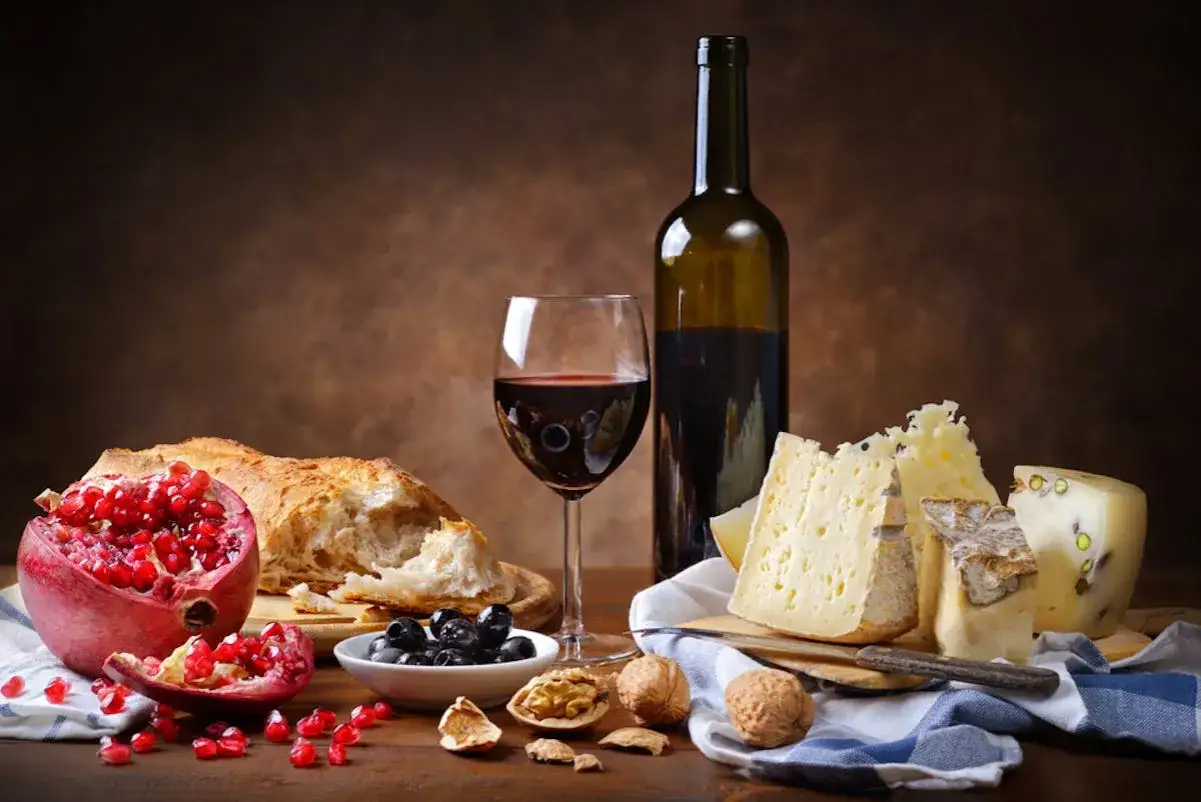 Primitivo kuchnia i wino: kieliszek czerwonego wina, butelka, chleb, ser, granat, oliwki i orzechy na drewnianym stole.