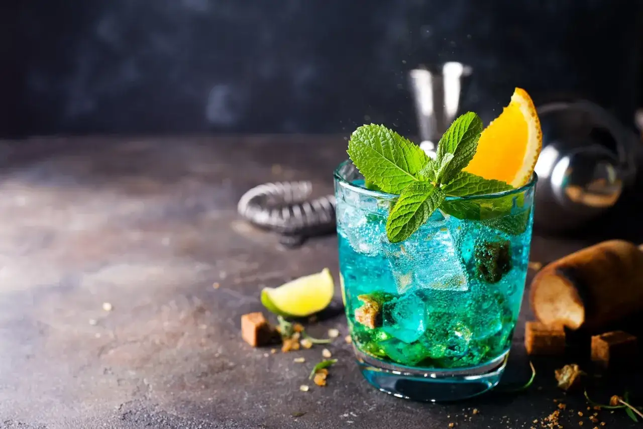Orzeźwiający drink z blue curacao i sprite, udekorowany miętą i plasterkiem pomarańczy. Idealny na letnie wieczory.