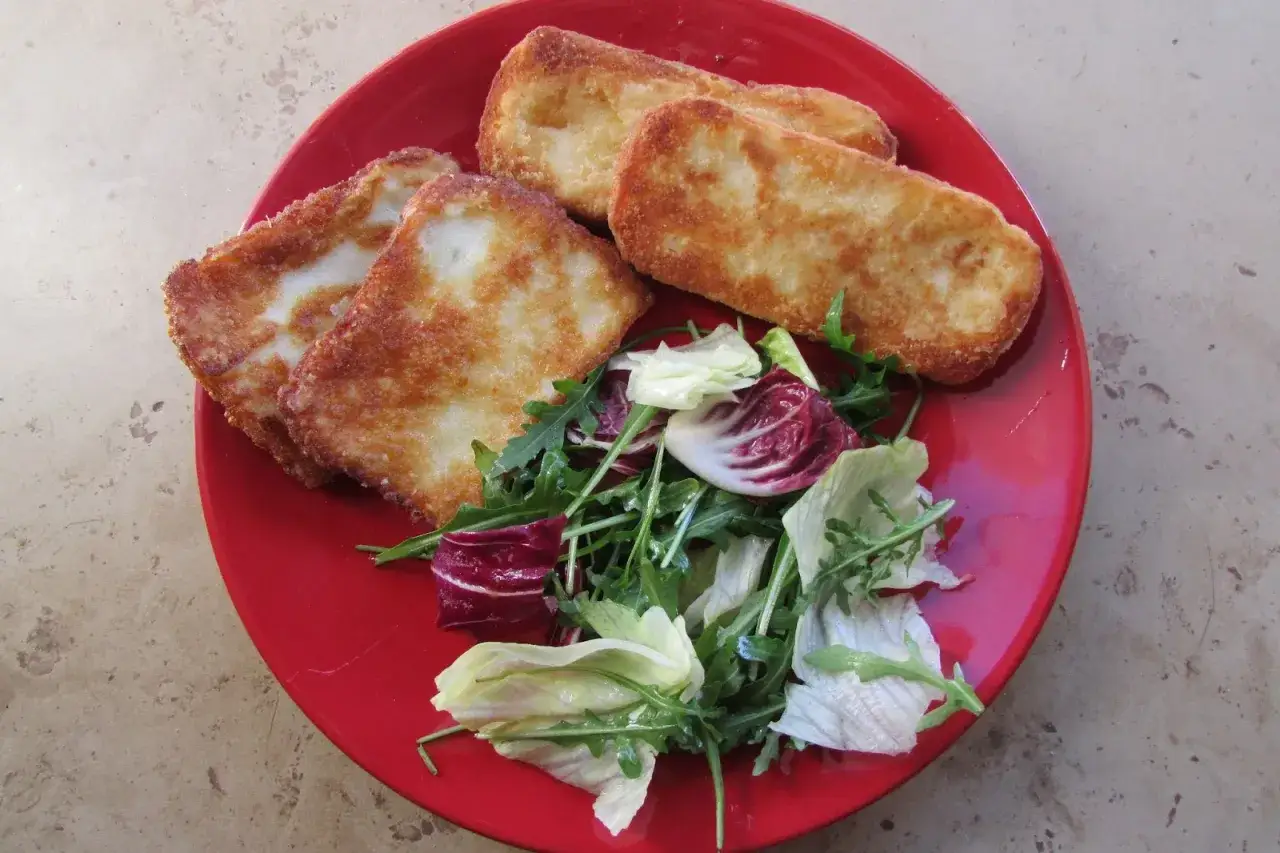 Złociste kawałki sera halloumi na czerwonym talerzu, podane z kolorową sałatką.