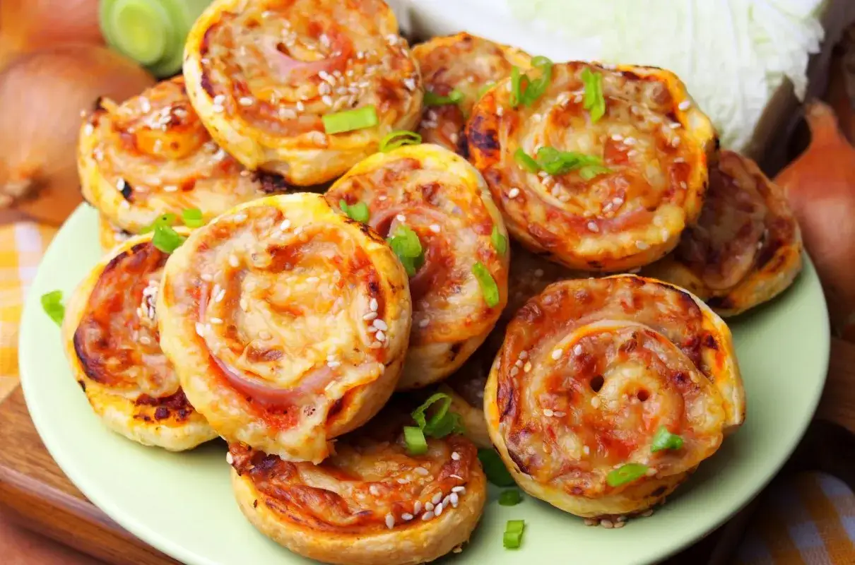 Pyszne pizzerinki z ciasta francuskiego, posypane sezamem i szczypiorkiem, prezentują się apetycznie na talerzu.