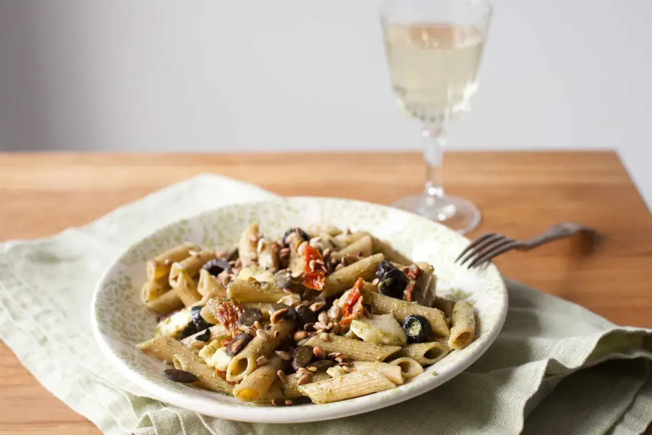 Penne z pesto, czarnymi oliwkami, kawałkami sera i suszonymi pomidorami, posypane pestkami słonecznika.