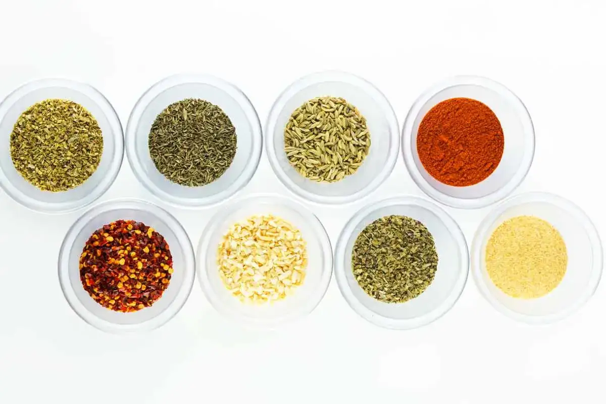 Osiem miseczek z przyprawami: oregano, tymianek, koper włoski, papryka, płatki chili, czosnek granulowany, bazylia, czosnek w proszku. Idealne jakie przyprawy do pizzy.