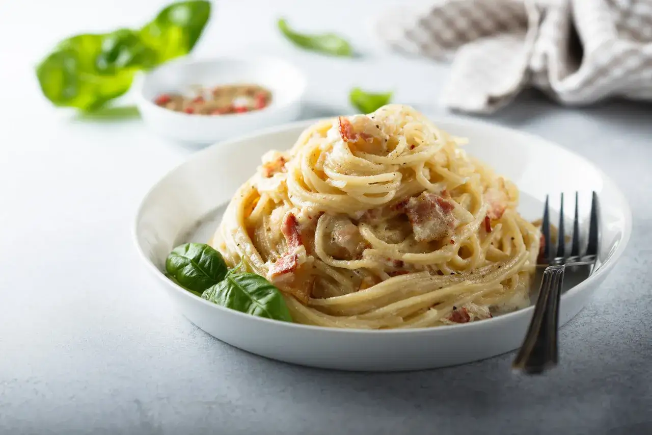 Pyszne spaghetti carbonara z boczkiem i bazylią. Idealna śmietana do carbonara sprawia, że danie jest kremowe.