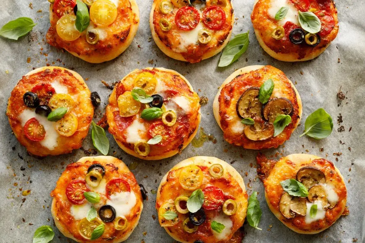 Pizzerinki z ciasta francuskiego, ozdobione pomidorkami, oliwkami i bazylią, wyglądają apetycznie.
