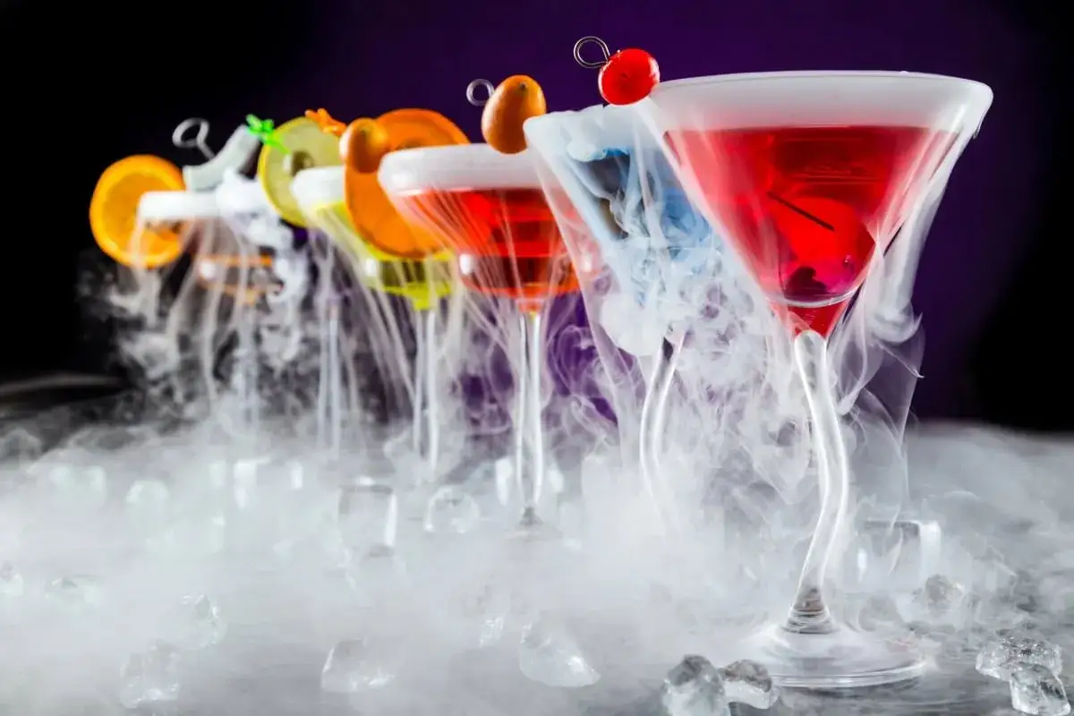 Rząd kolorowych drinków z owocami, otoczonych gęstą mgłą suchego lodu, tworzy magiczną atmosferę.