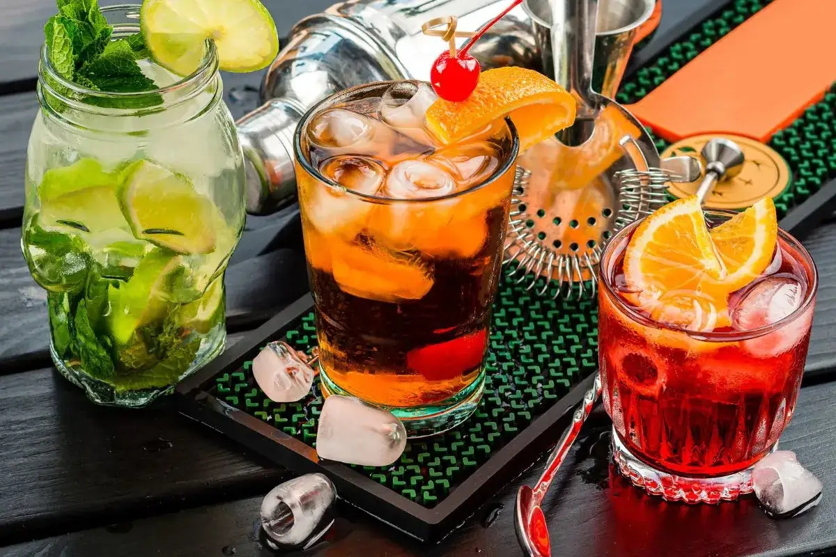 Trzy orzeźwiające drinki: jeden z wódką, limonką i miętą, drugi z wiśnią i pomarańczą, trzeci czerwony z pomarańczą.