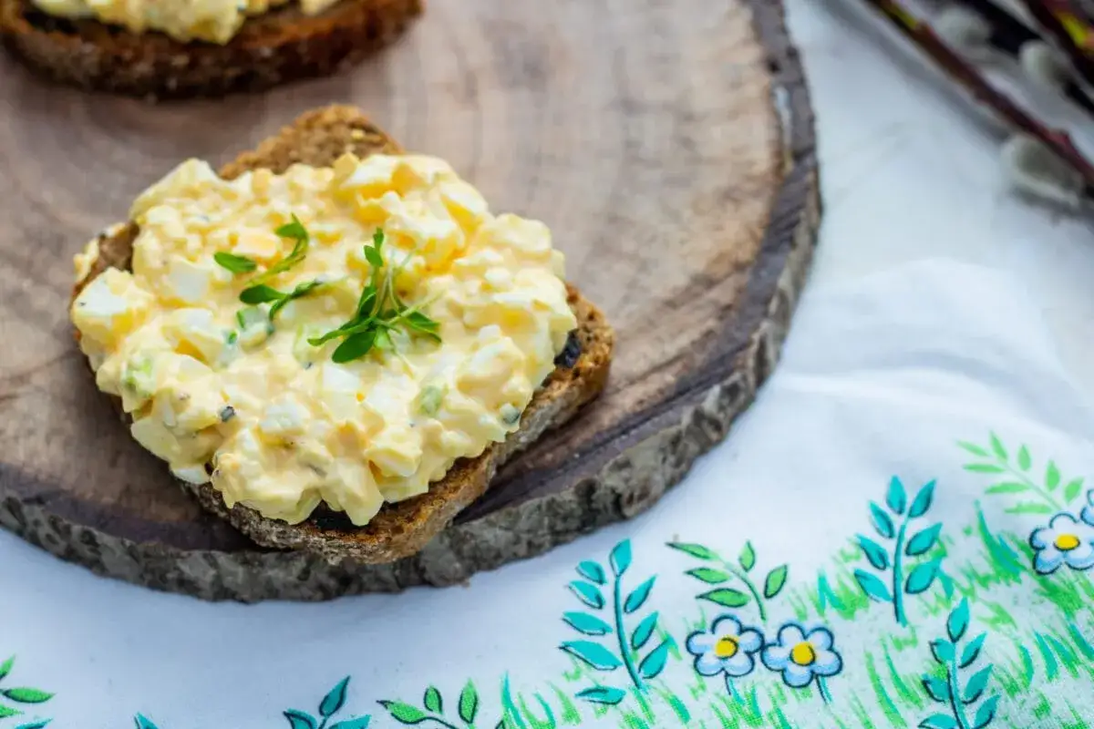 Pyszna pasta jajeczna na ciemnym pieczywie, udekorowana świeżymi ziołami. Idealna na śniadanie lub przekąskę, pokazuje pasta jajeczna na różne sposoby.