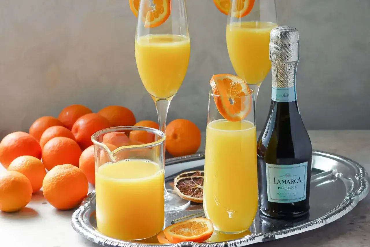 Dwa kieliszki orzeźwiającego mimoza drink, świeże pomarańcze i butelka prosecco na tacy. Idealny na brunch!