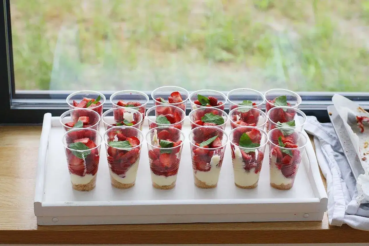 Mini deserki z mascarpone i truskawkami, udekorowane listkami mięty, gotowe do podania na tacy.