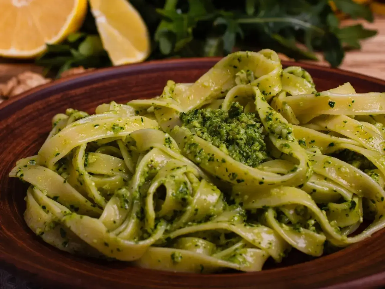 Pappardelle z aromatycznym makaronem z pesto, podane na glinianym talerzu, z cytryną i rukolą w tle.