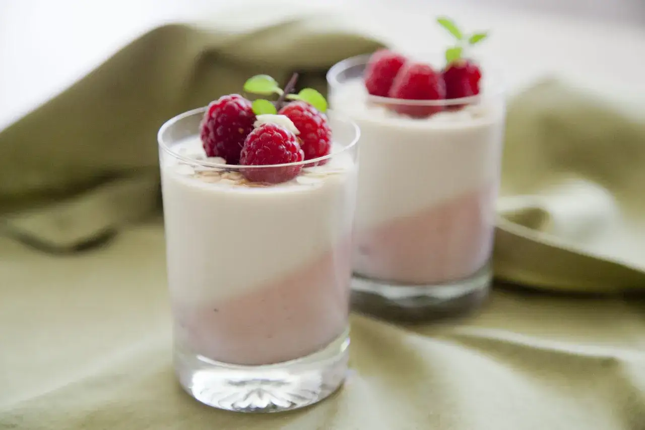 Dwa deserki panna cotta z malinami i miętą, udekorowane płatkami migdałów.