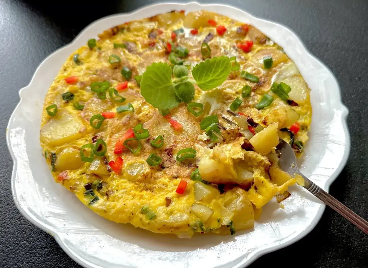 Pyszna frittata z ziemniakami, papryką i szczypiorkiem, udekorowana świeżymi ziołami. Idealna na śniadanie lub lekki obiad.