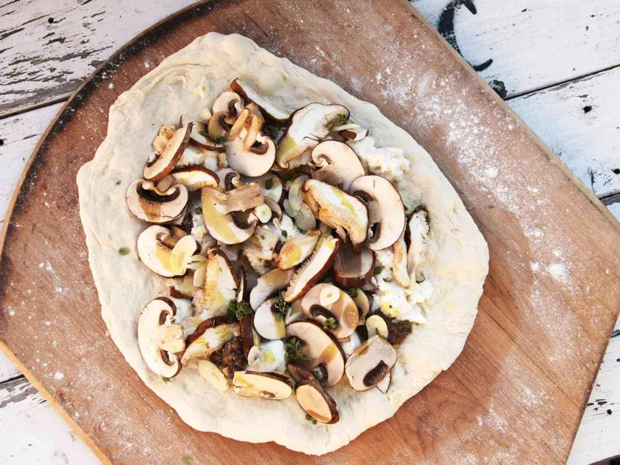 Surowe pieczarki na pizze, pokrojone w plasterki, ułożone na cieście z serem i ziołami.