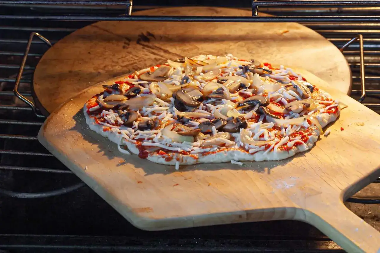 Pizza z pieczarkami i cebulą na desce, gotowa do włożenia do pieca. Czas piec pizzę w 200 stopniach!