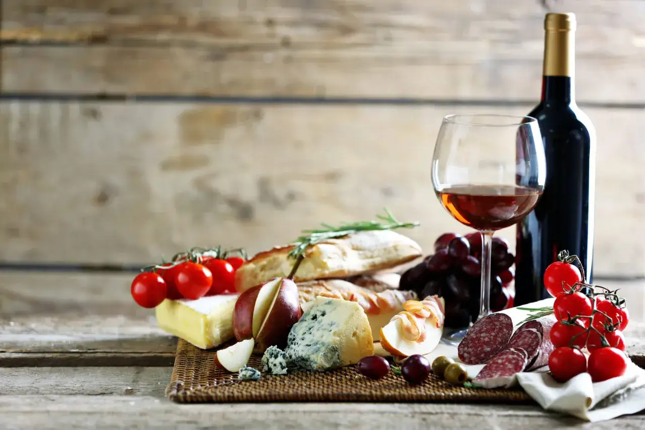 Primitivo kuchnia i wino: kieliszek wina, butelka, sery, wędliny, bagietka, pomidorki i winogrona na drewnianym stole.