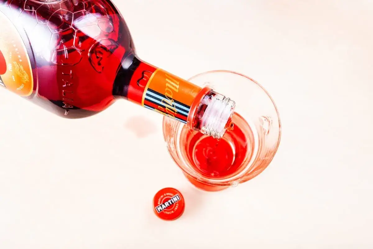 Czerwony Martini Rosso leje się do kieliszka, tworząc idealne drinki. Obok leży czerwona zakrętka.