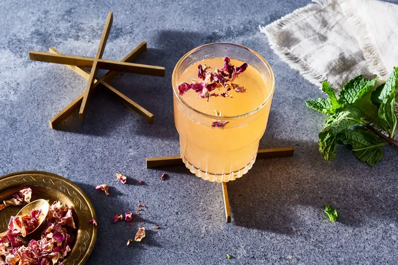 Elegancki drink z płatkami róży, idealny do domowych przepisów na drinki. Obok świeża mięta i ozdobne elementy.