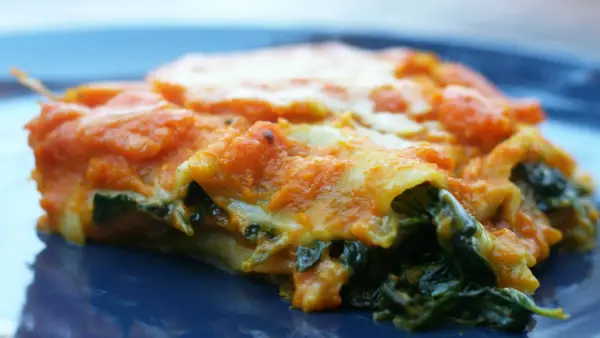 Pyszne lasagne ze szpinakiem, z pomarańczowym sosem i ciągnącym się serem, na granatowym talerzu.