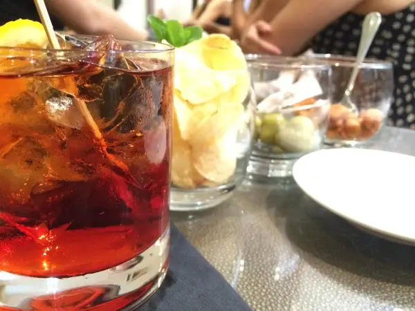 Czerwony drink z lodem i cytryną, obok chipsy i oliwki. Idealny na aperitif, jak zrobic martini?