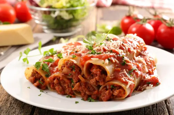Pyszne cannelloni z mięsem mielonym, polane sosem pomidorowym i posypane parmezanem, na talerzu z pomidorami i sałatką.