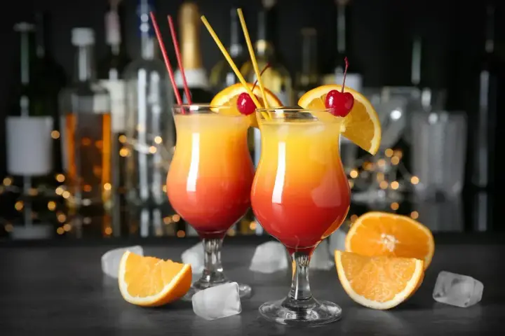 Dwa drinki z wódką, ozdobione pomarańczą i wiśnią, na tle barowych butelek. Idealne na letnie wieczory.