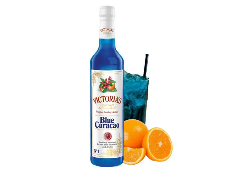 Syrop Blue Curacao Victoria's, idealny do drinków. W szklance niebieski koktajl z lodem i słomką, obok pomarańcze.